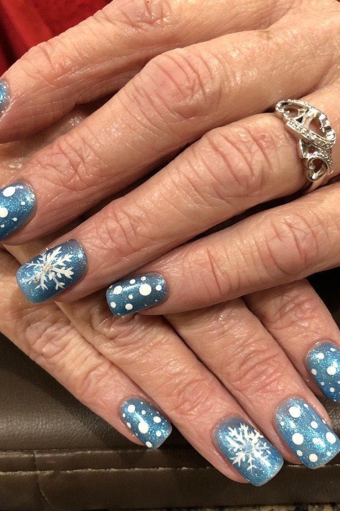 Soft dusty blue nails with delicate white snowflakes on mature hands, calm winter look