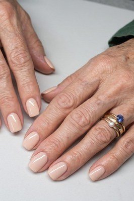 Sheer nude nail polish on very short natural nails, mature woman hands