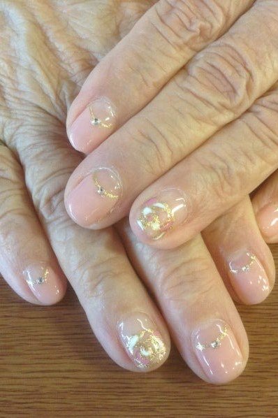 Sheer nude nails with gold glitter tips on very mature hands