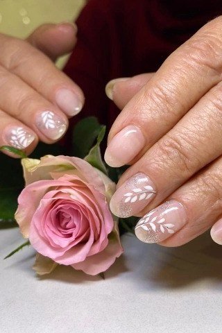 White floral lace nail art on nude nails, mature hands