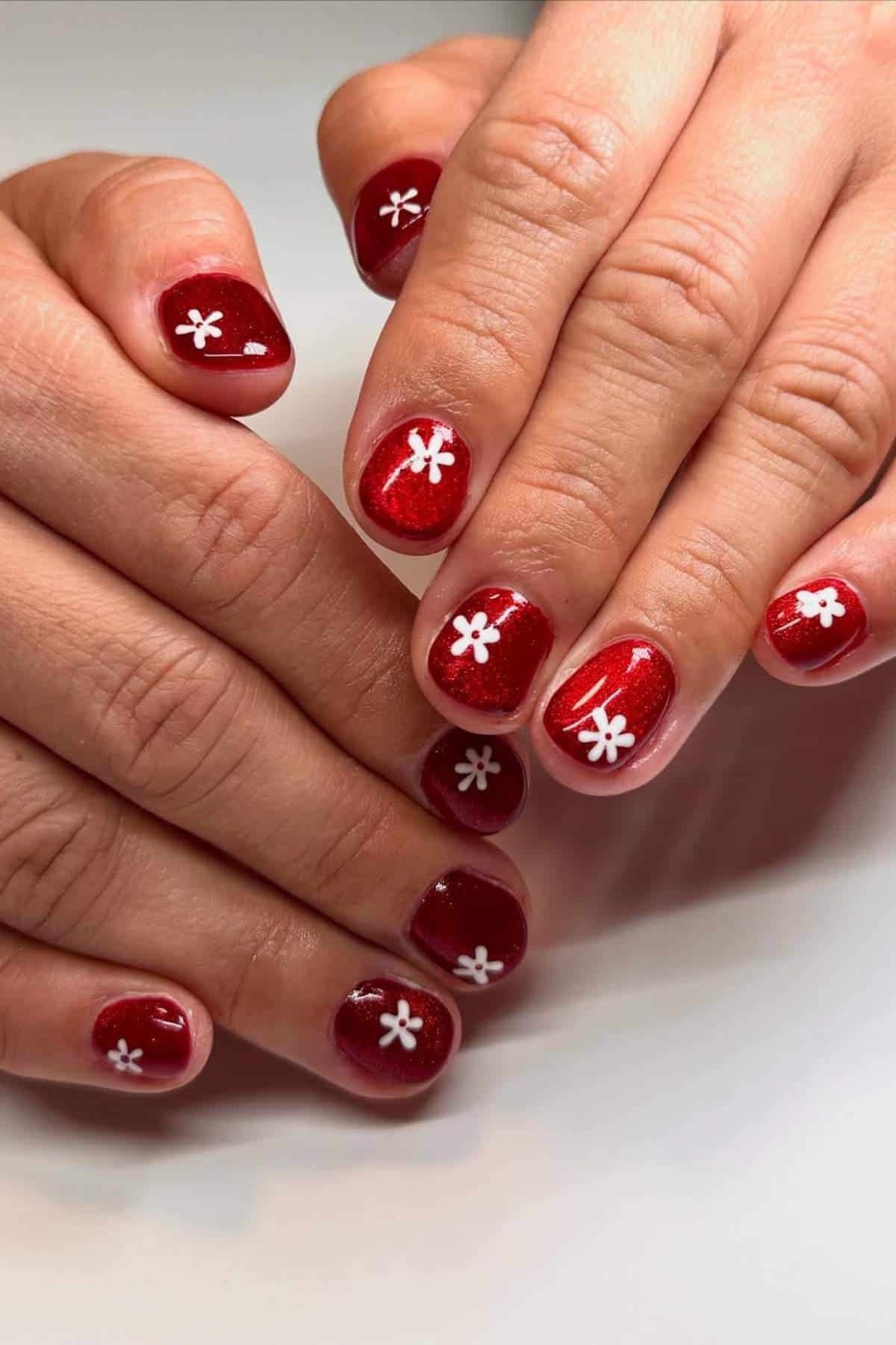 Red shimmer nails with white daisy nail art, cute summer floral nails for women over 40