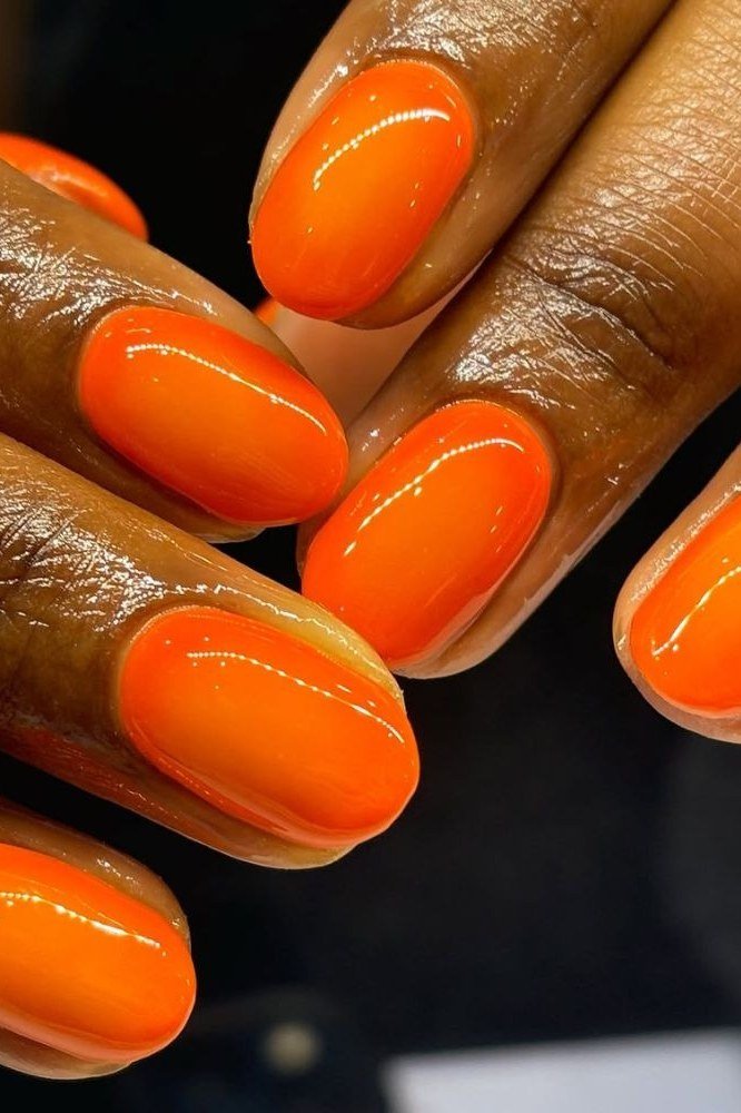 Bright orange oval nails with glossy finish on dark skin tone, bold summer nails