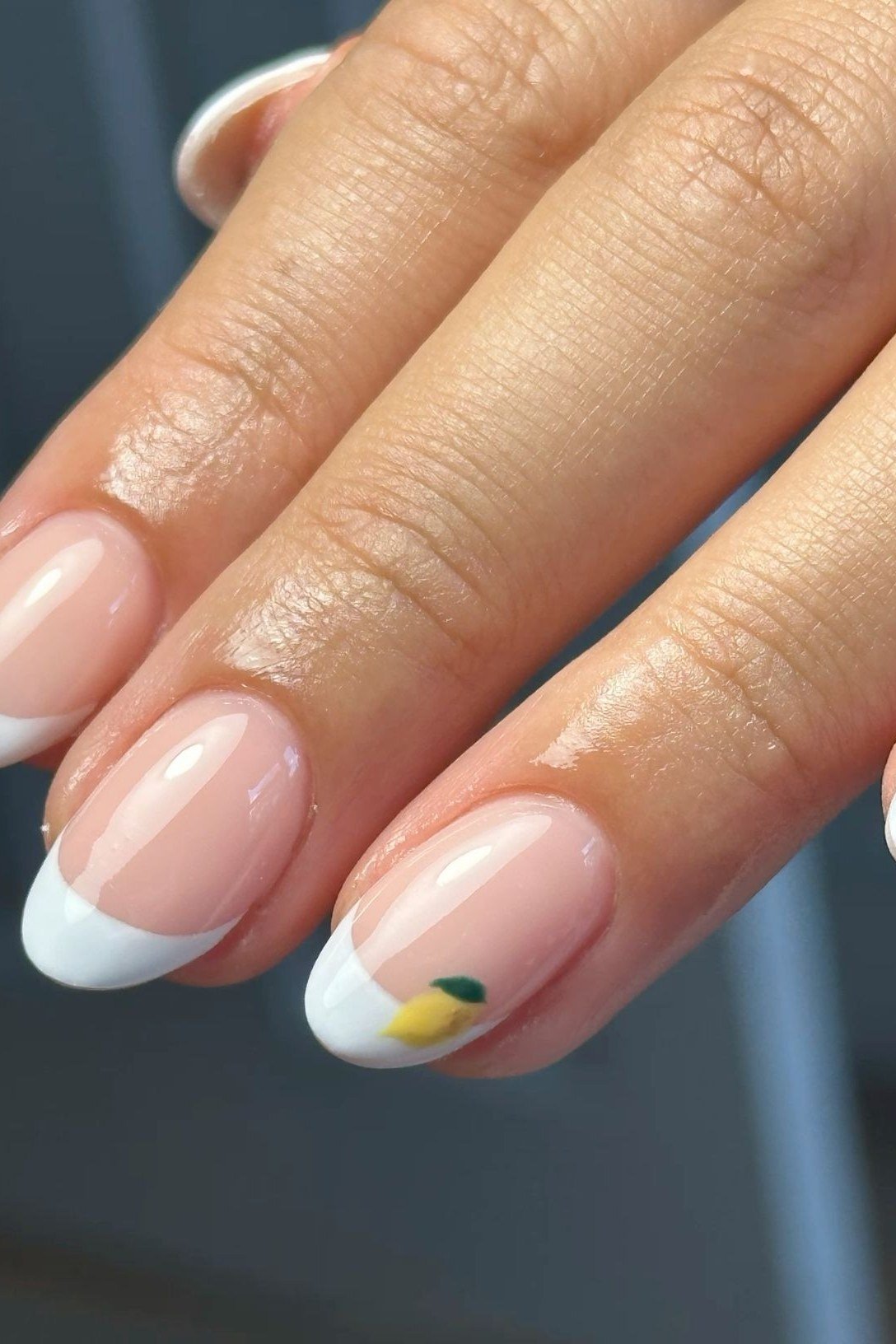 Nude almond nails with white French tips and tiny lemon nail art accent, citrus summer French nails