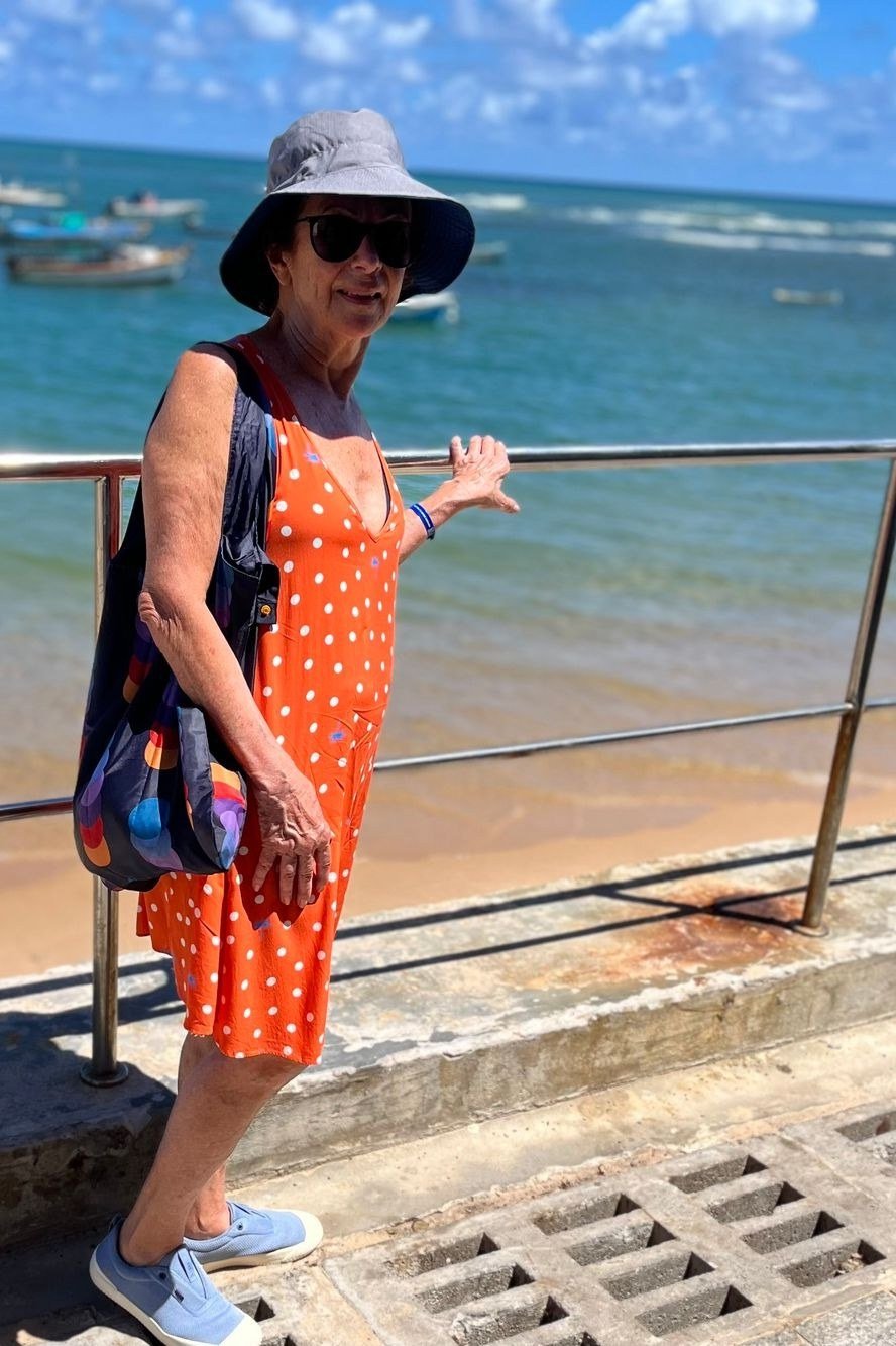 Older woman wearing orange polka dot midi sundress at beach, sunglasses - summer sundresses for women over 60