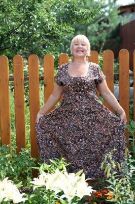 Older woman wearing dark floral maxi dress by wooden fence - summer sundresses for women over 60