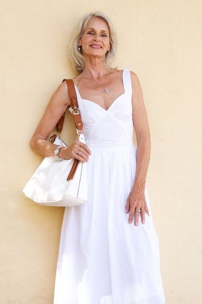 Older woman wearing white maxi sundress, cream wall - summer sundresses for women over 60