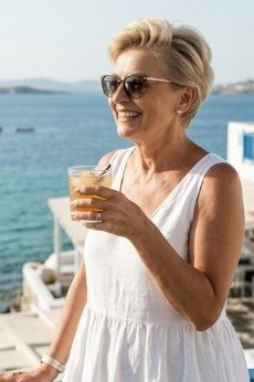 Older woman wearing white sundress at Greek coast, drink - summer sundresses for women over 60