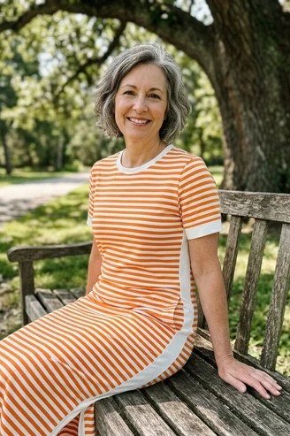 Older woman wearing gray hair, orange striped maxi dress on bench - summer sundresses for women over 60