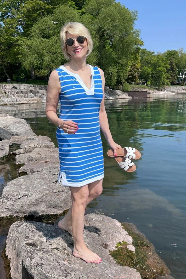 Older woman wearing blue white striped sleeveless sundress on rocks by water - summer sundresses for women over 60
