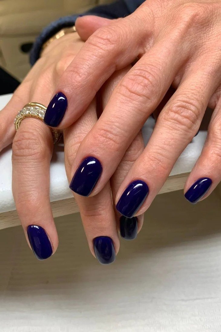 Classic navy blue nails on mature hands with gold rings