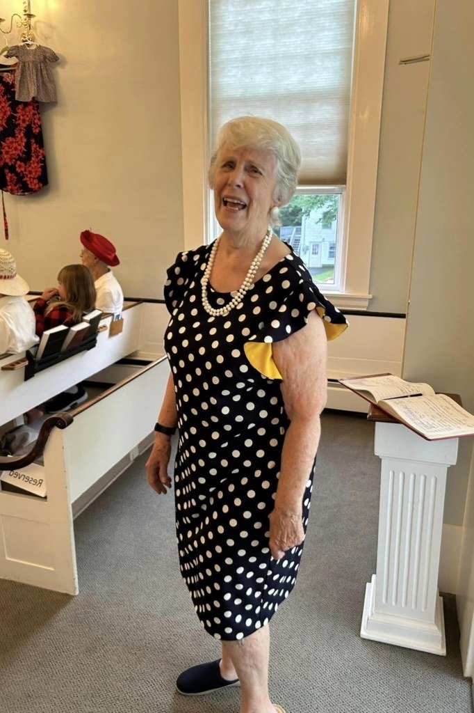 Older woman wearing black and white polka dot midi dress, church interior, a timeless casual outfit for women over 60.