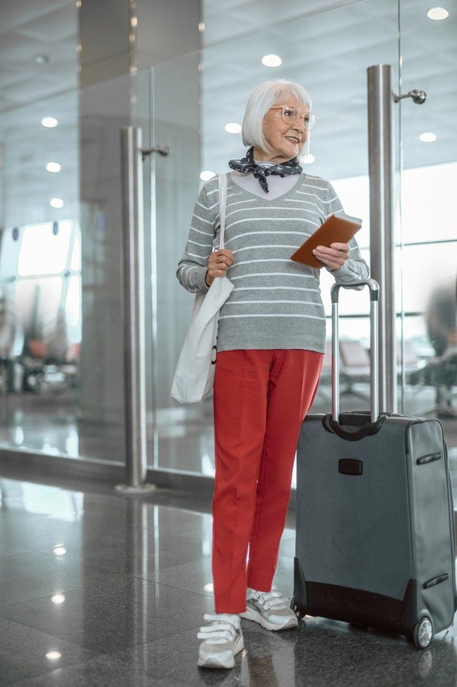 Older woman wearing gray striped top and red wide pants and white sneakers, airport, a timeless casual outfit for women over 60.