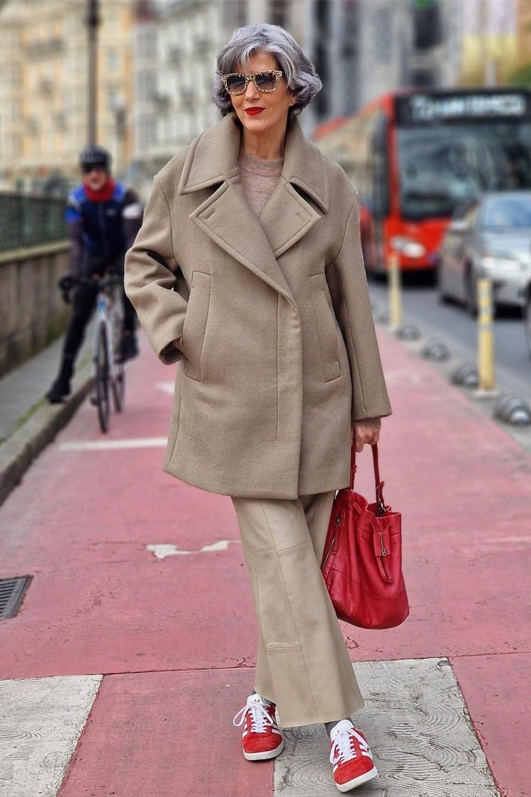 Older woman wearing beige oversized coat and red handbag, red bike lane, a timeless casual outfit for women over 60.