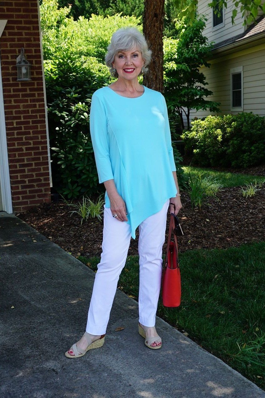 Older woman wearing turquoise tunic and white slim pants, suburban home, a timeless casual outfit for women over 60.