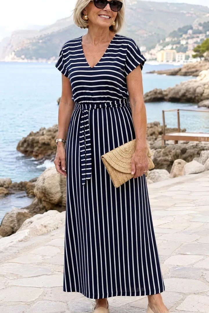 Older woman wearing navy and white striped maxi dress and clutch, seaside promenade, a timeless casual outfit for women over 60.