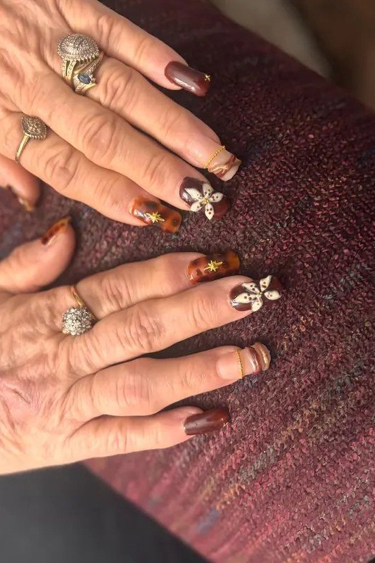 Burgundy nails with rhinestone flower accents on mature hands