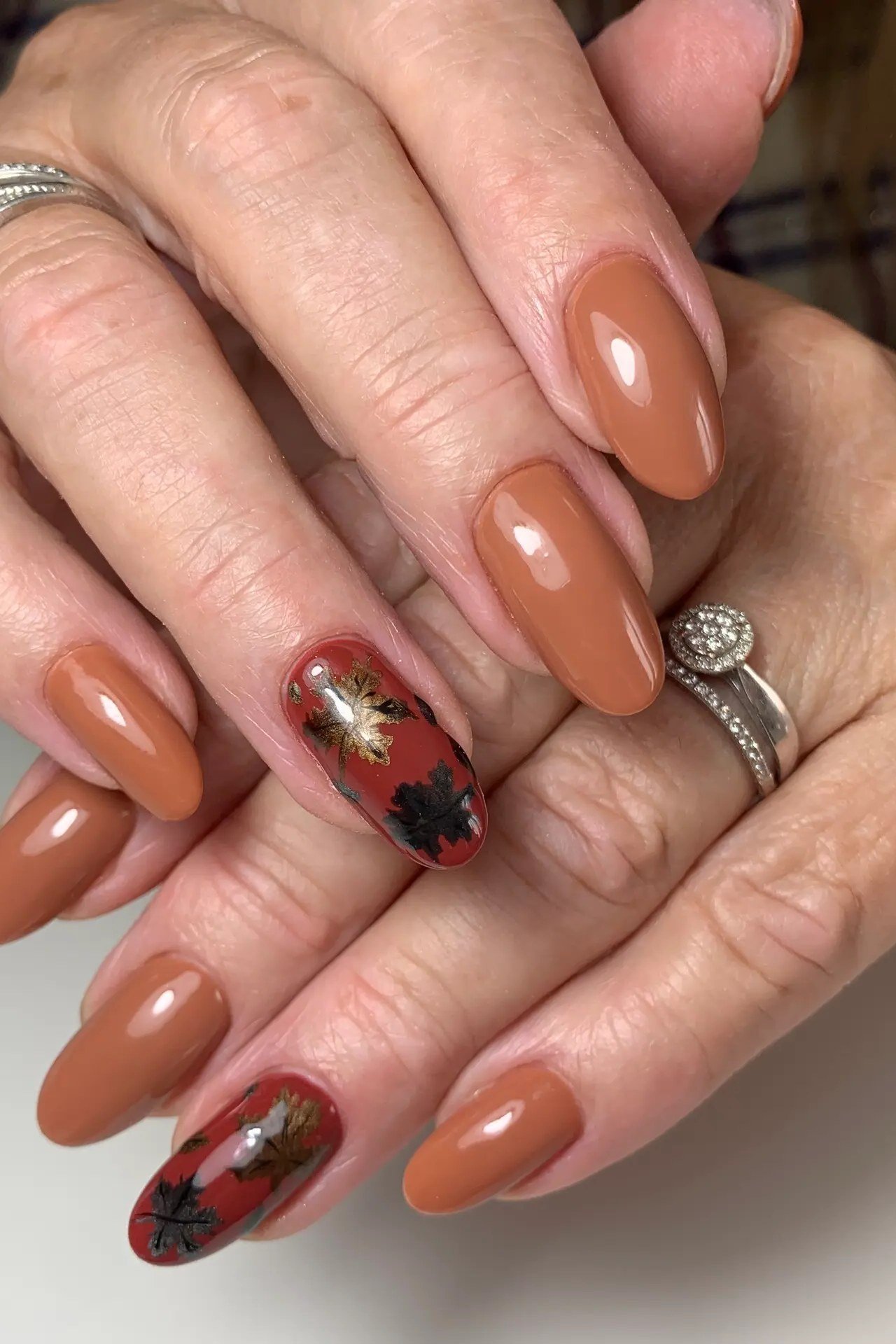 Caramel nails with fall leaf art on mature hands