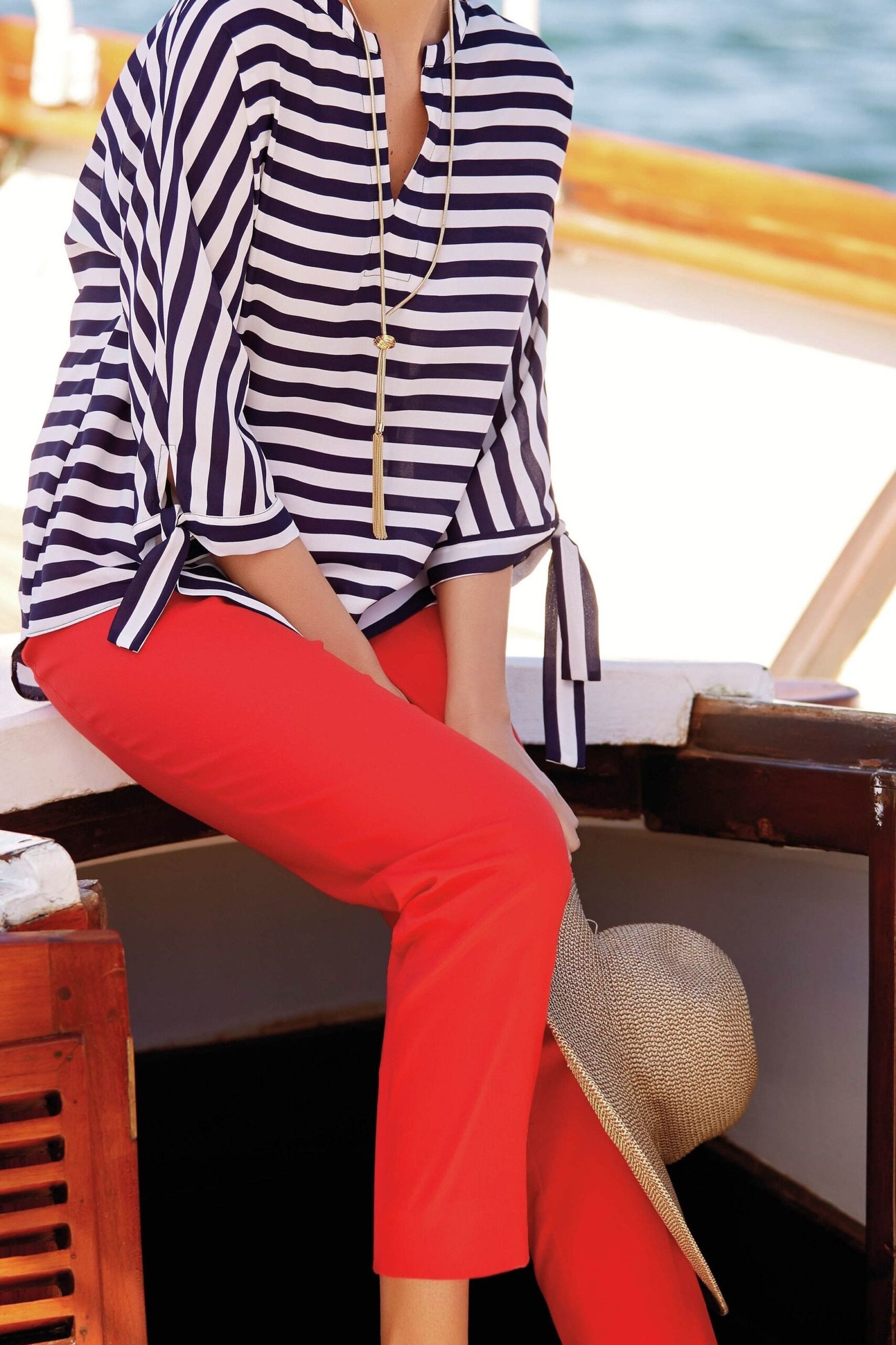 Navy-and-white striped tee with bright red cropped pants and white sandals, seated on a cruise ship deck; classic bold color-block cruise outfit - travel outfit for women over 50