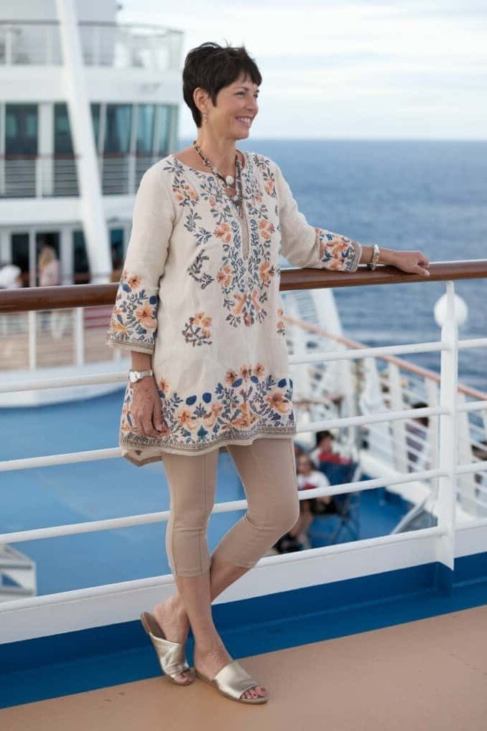 White embroidered boho tunic dress with gold flat sandals, by a cruise ship pool; airy white-on-white resort cruise style - travel outfit for women over 50