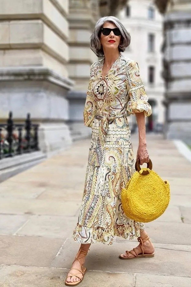 Cream paisley midi dress with flutter sleeves and a round yellow woven bag, by stone columns; statement-print dress for warm city days - travel outfit for women over 50
