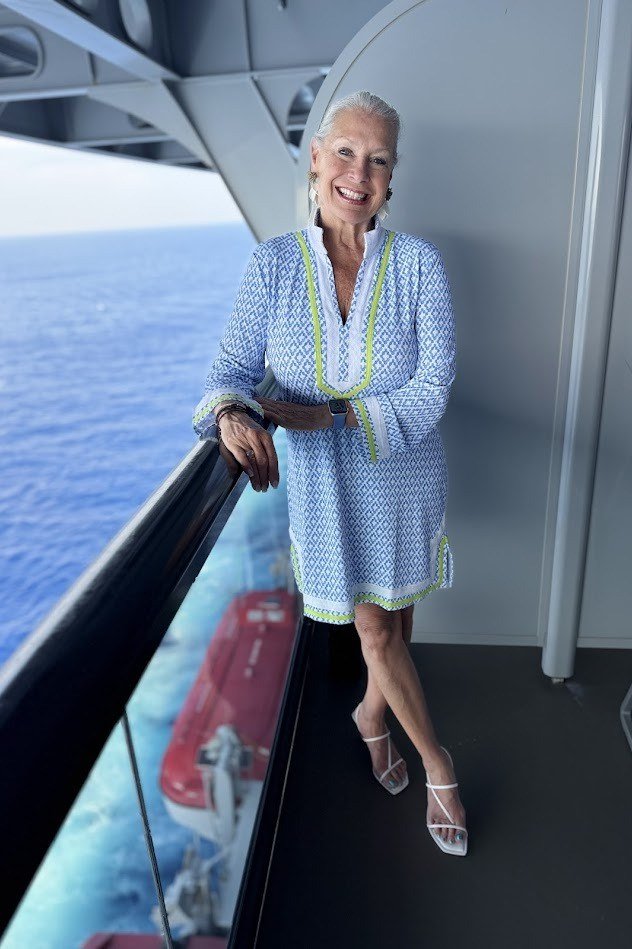 Light blue patterned mini dress with pockets and white heeled sandals, standing on a cruise ship balcony; fresh pastel cruise dress - travel outfit for women over 50