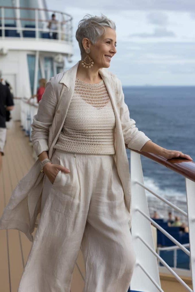 Cream striped knit top with wide-leg cream linen pants, leaning on a cruise ship railing; tonal cream resort set - travel outfit for women over 50