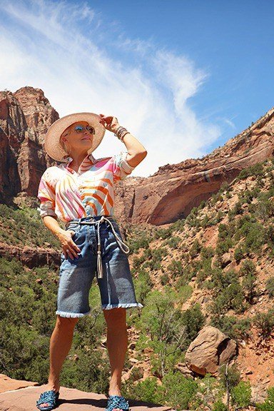 Orange-and-white striped tee with denim shorts, a straw hat, and blue sneakers, at a desert canyon overlook; national park hiking-casual outfit - travel outfit for women over 50