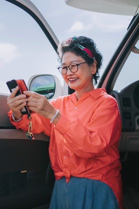 Coral button shirt with turquoise wide-leg pants and sunglasses, sitting in a car doorway; colorful cheerful road trip outfit - travel outfit for women over 50