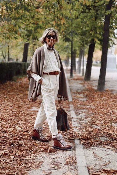 Gray knit poncho over a white top and white pants with red ankle boots, on a leaf-covered park path; poncho fall statement look - travel outfit for women over 50