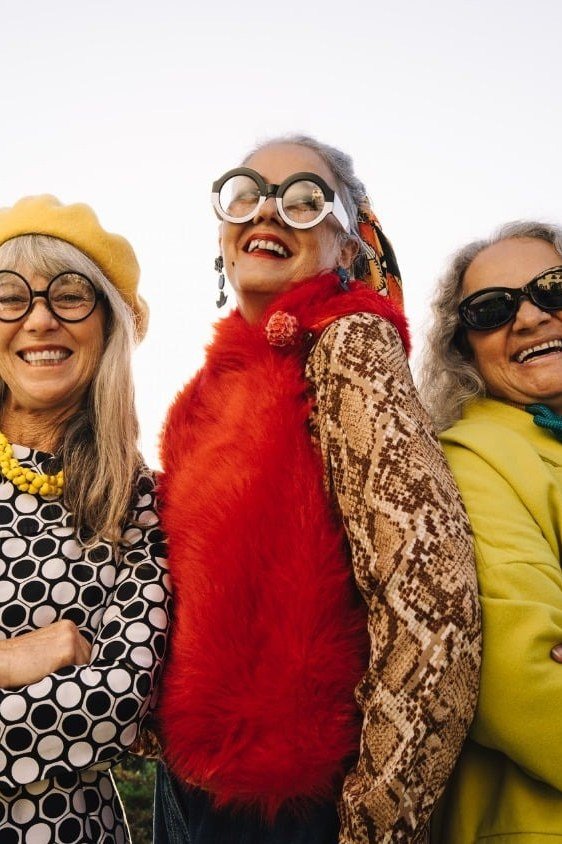 Three women in colorful statement coats together - trendy outfits for women over 70