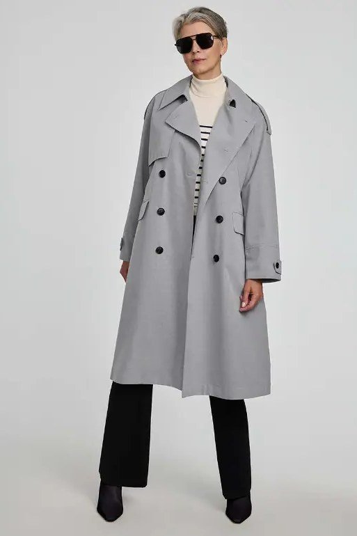 Fall turtleneck outfit for women over 50: gray trench coat over striped top and cream turtleneck, black pants, studio