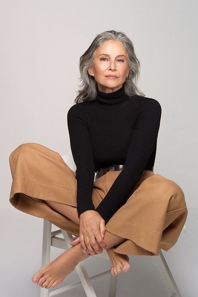 Fall turtleneck outfit for women over 50: black turtleneck with camel wide pants, seated, studio