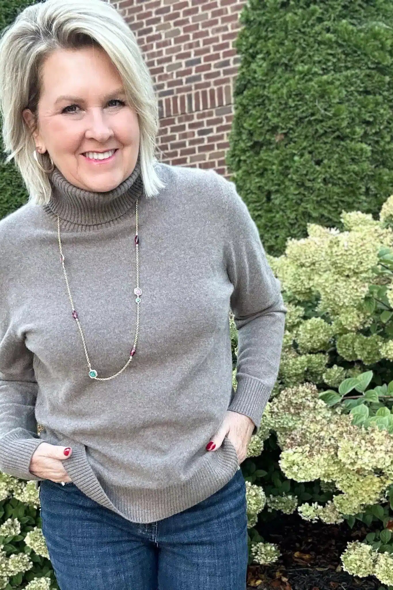 Fall turtleneck outfit for women over 50: taupe turtleneck with long necklace, jeans, close-up