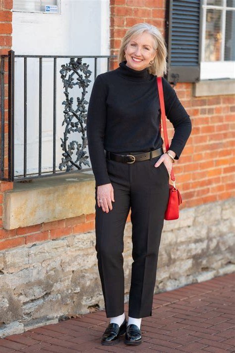 Fall turtleneck outfit for women over 50: navy turtleneck with black trousers, red bag, brick wall