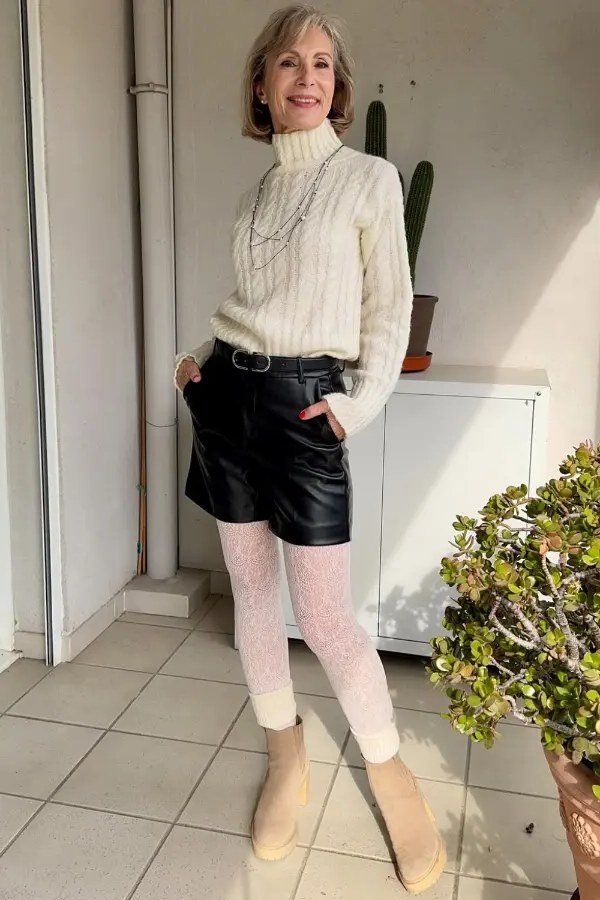 Fall turtleneck outfit for women over 50: cream cable turtleneck with black leather shorts, lace tights, patio