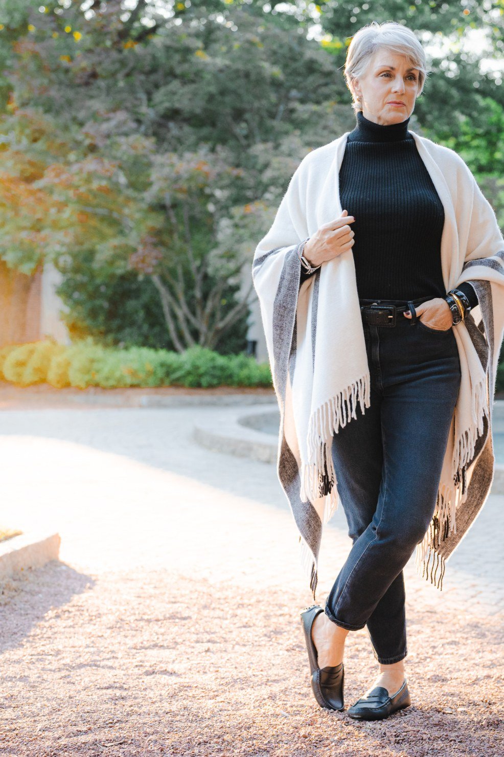 Fall turtleneck outfit for women over 50: white cable turtleneck poncho with burgundy bag, garden