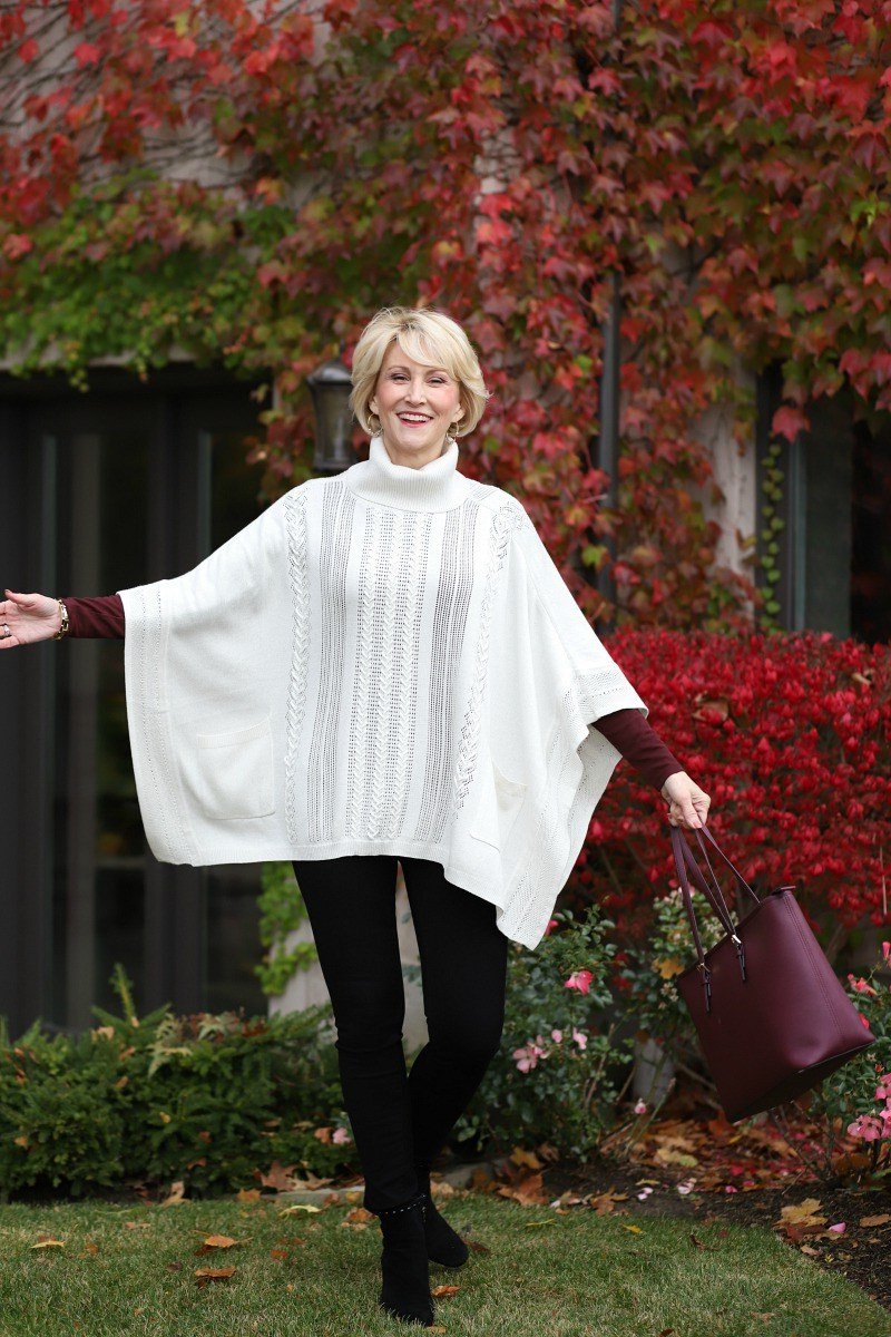 Fall turtleneck outfit for women over 50: white cable turtleneck poncho over burgundy turtleneck, black pants