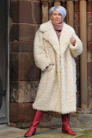 Winter outfit idea 22 for women over 60: cream shearling coat with red boots, stone building