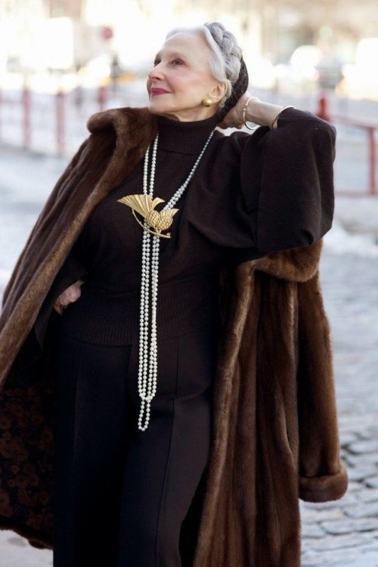 Winter outfit idea 26 for women over 60: brown fur coat with black dress and long pearls, street
