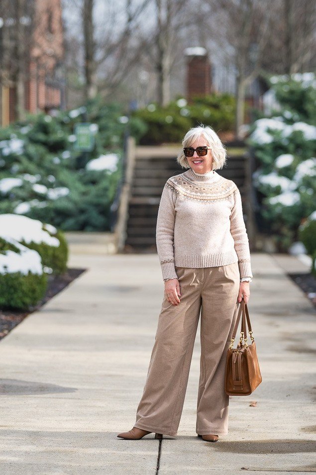 Winter outfit idea 41 for women over 60: cream knit top with wide trousers, snowy garden