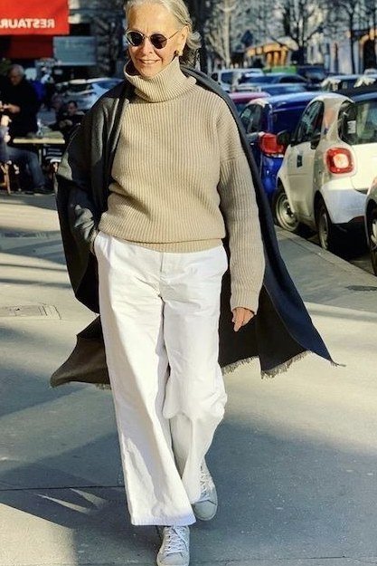 Winter outfit idea 44 for women over 60: camel sweater with white pants, black coat over shoulders