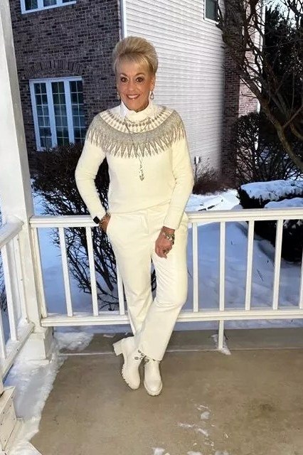 Woman over 60 wearing cream fair isle knit sweater with matching wide trousers and cream ankle boots