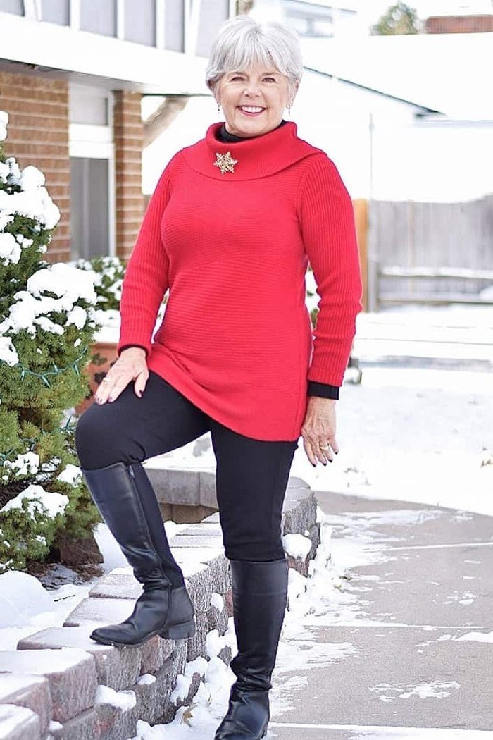 Older woman in red turtleneck sweater dress with black leggings and black knee high boots