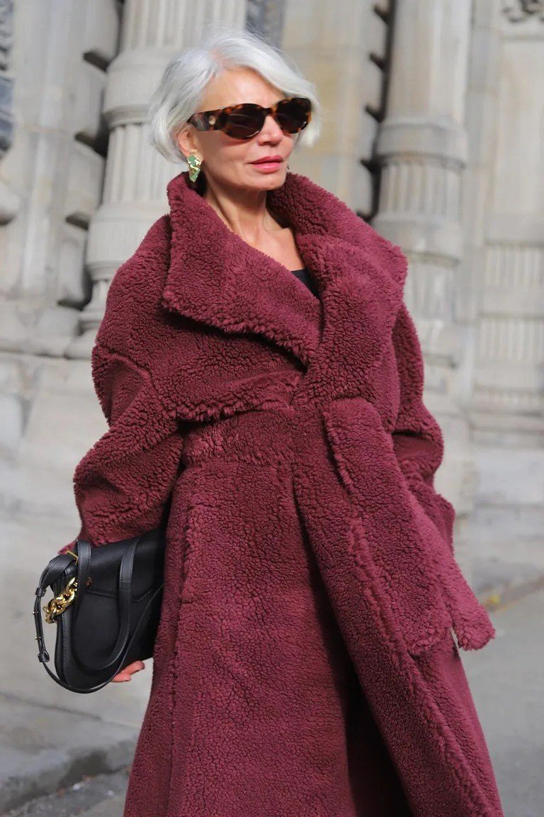 Older woman wearing burgundy teddy long coat with black handbag