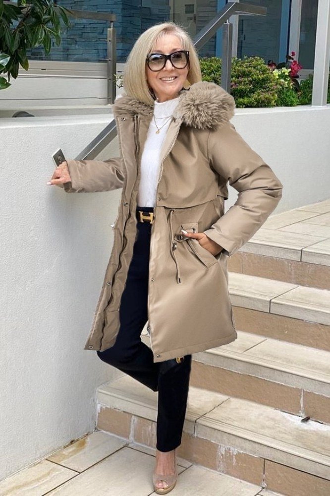 Woman over 60 wearing camel coat with faux fur collar, white turtleneck and beige heels