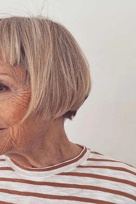 Ash-blonde pixie-bob with bangs, side view, striped top - wash and wear haircut for women over 60