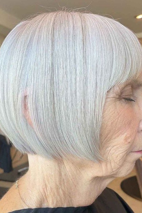 White sleek wedge with bangs on a woman over 60, salon side view - wedge bob hairstyle