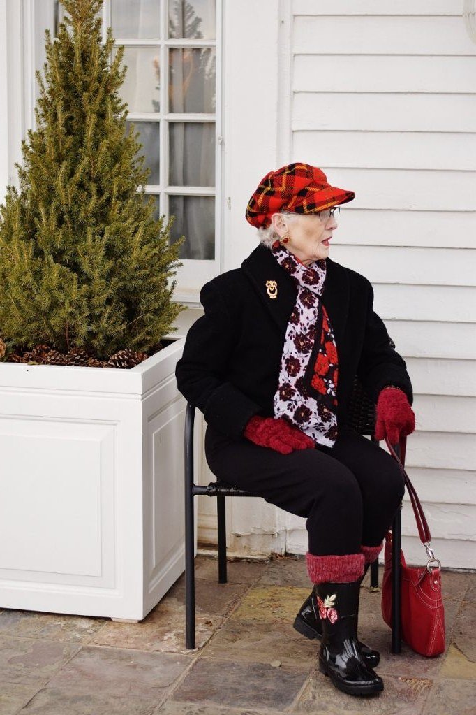 Winter outfit for women over 60: older woman seated, red beret, black wool coat, red scarf, red gloves, red handbag