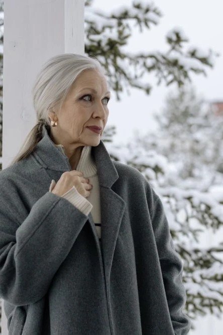 Winter outfit for women over 60: gray wool coat, snowy background, side-profile winter portrait