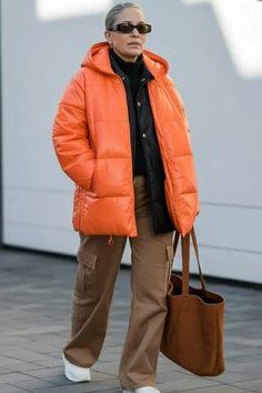 Winter outfit for women over 60: orange puffer jacket, brown wide pants, brown tote